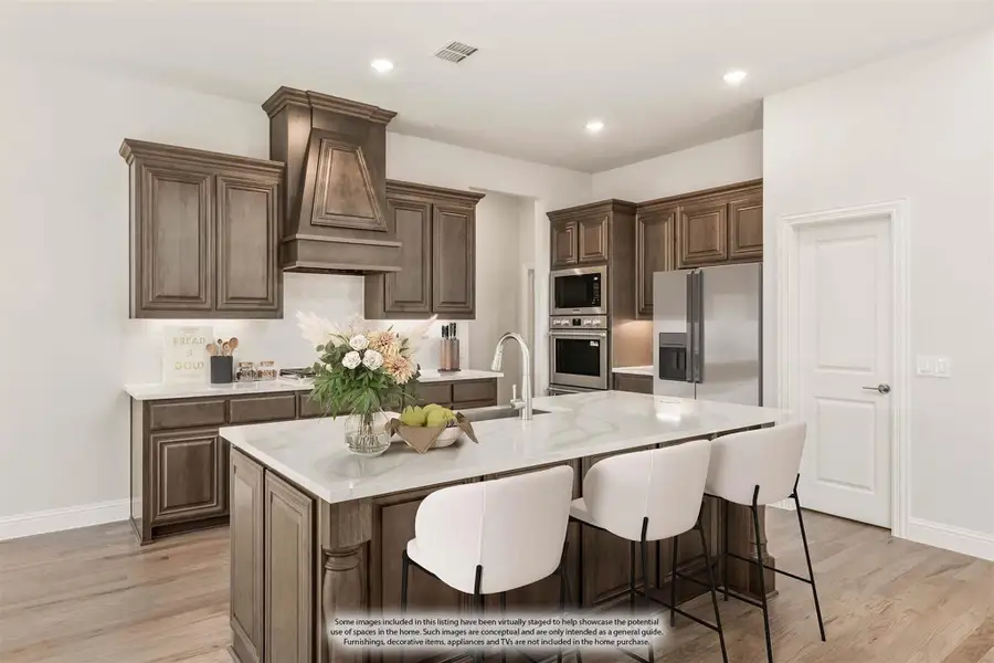 Kitchen with dark wood cabinets, large center island with white countertop, and stainless steel appliances including double oven and refrigerator