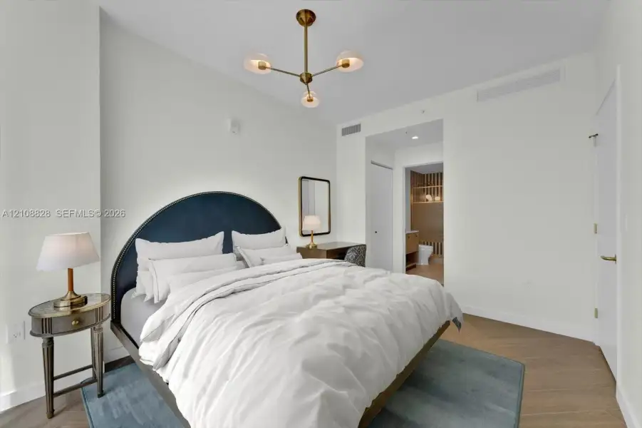 Modern bedroom featuring wood-finish flooring, a multi-arm brass finish chandelier, and neutral wall color
