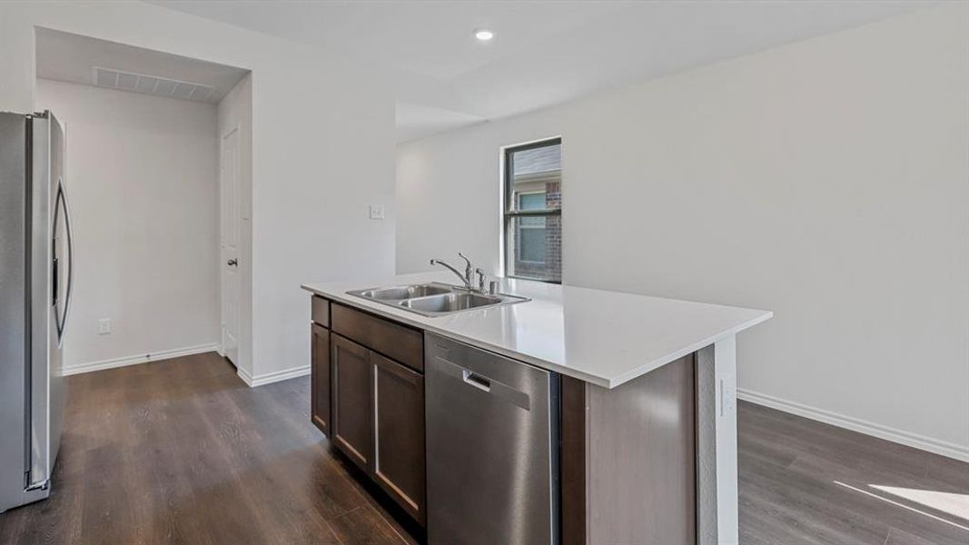 Kitchen featuring stainless steel appliances, light countertops, a center island with sink, dark wood-style flooring, and recessed lighting Kitchen featuring stainless steel appliances, light countertops, a center island with sink, dark wood-style flooring, and recessed lighting