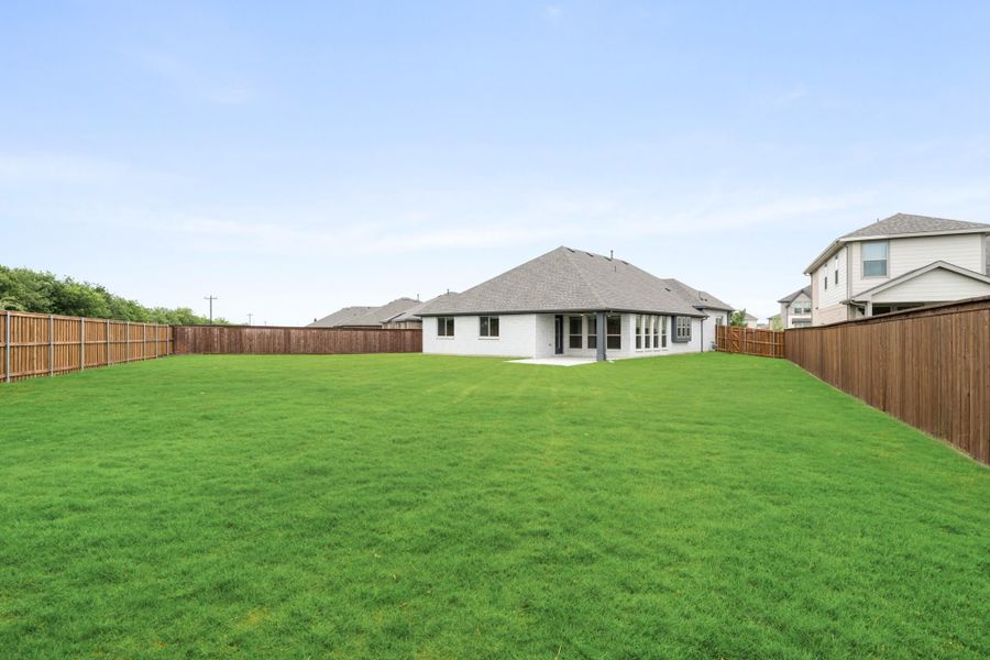 Large fenced backyard with green lawn and single-story home with covered patio in background Large fenced backyard with green lawn and single-story home with covered patio in background