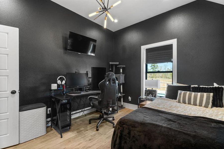 Bedroom with an inviting chandelier, vaulted ceiling, wood finished floors, a textured wall, and baseboards Bedroom with an inviting chandelier, vaulted ceiling, wood finished floors, a textured wall, and baseboards