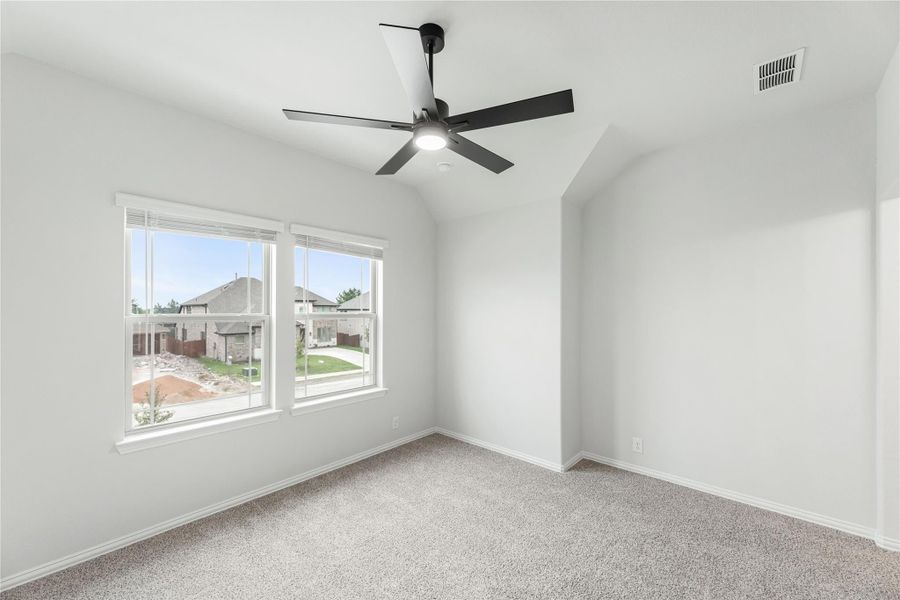 Empty bedroom with vaulted ceiling, black ceiling fan, carpet flooring, and two windows with neighborhood view Empty bedroom with vaulted ceiling, black ceiling fan, carpet flooring, and two windows with neighborhood view
