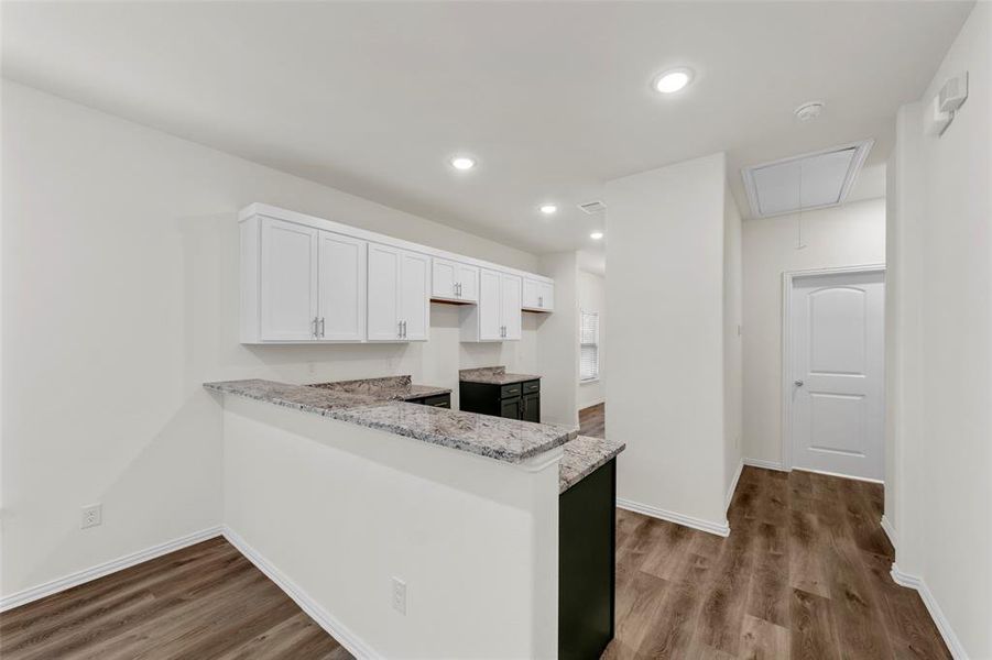 Kitchen with kitchen peninsula, white cabinetry, hardwood / wood-style flooring, and light stone countertops