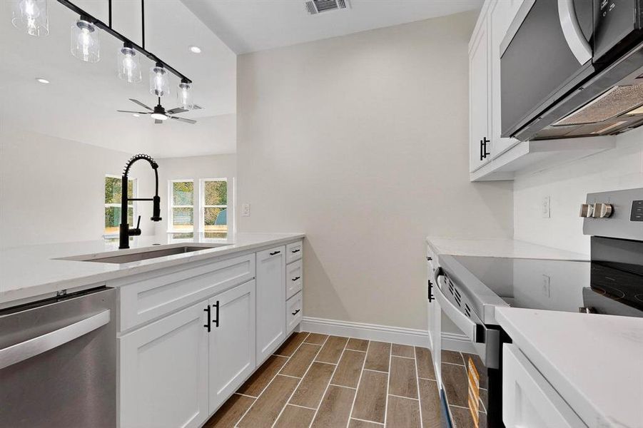Kitchen with appliances with stainless steel finishes, white cabinets, wood finish floors, light stone counters, and recessed lighting Kitchen with appliances with stainless steel finishes, white cabinets, wood finish floors, light stone counters, and recessed lighting