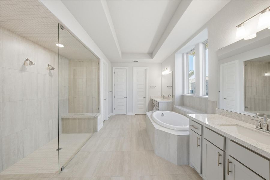 Bathroom featuring a garden tub, two vanities, a shower stall, light tile patterned flooring, and a tray ceiling