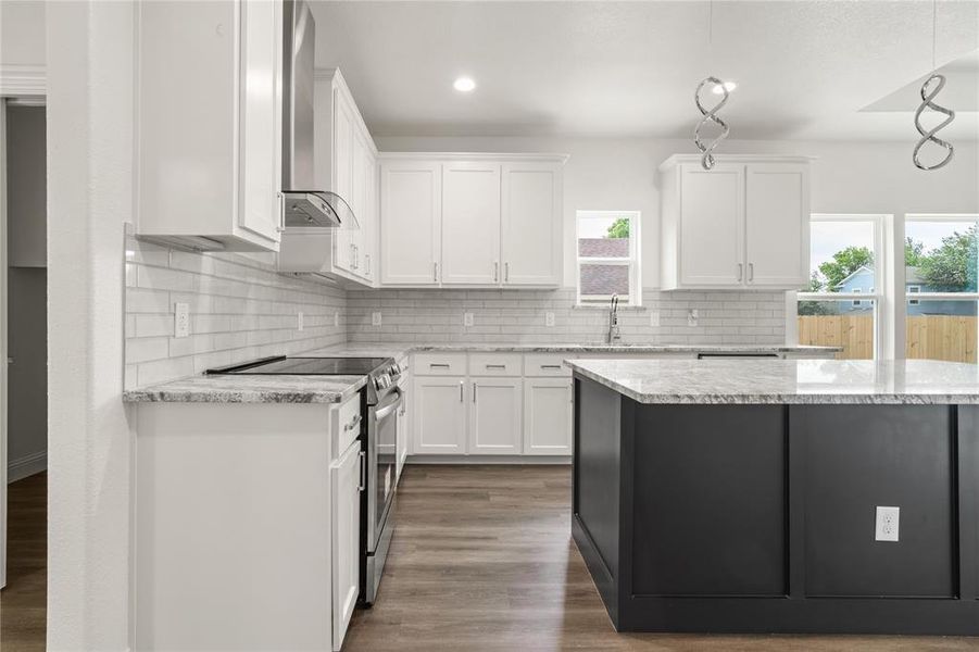 Kitchen featuring white shaker cabinetry, stainless steel appliances, light-toned countertops, subway tile backsplash, and a dark-toned island with integrated pendant lighting