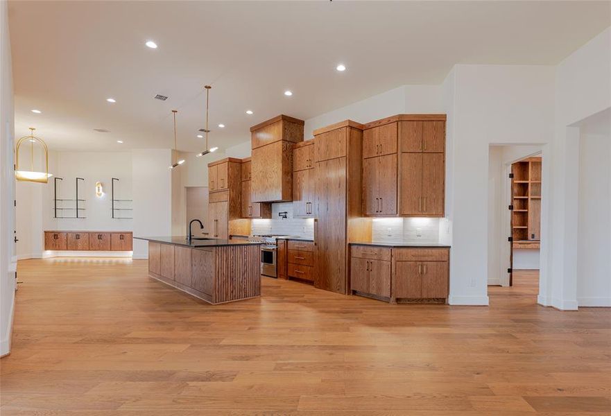 Kitchen with tasteful backsplash, a spacious island, open floor plan, high end range, and light wood-style flooring
