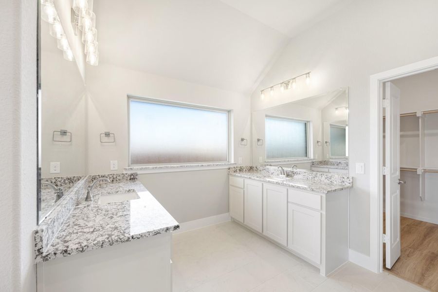 Master bathroom with dual vanities, granite countertops, vaulted ceiling, and walk-in closet access