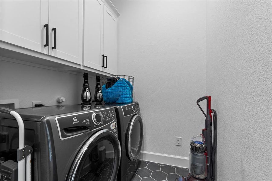 Laundry area with cabinet space, washer and clothes dryer, tile patterned flooring, and a textured wall Laundry area with cabinet space, washer and clothes dryer, tile patterned flooring, and a textured wall