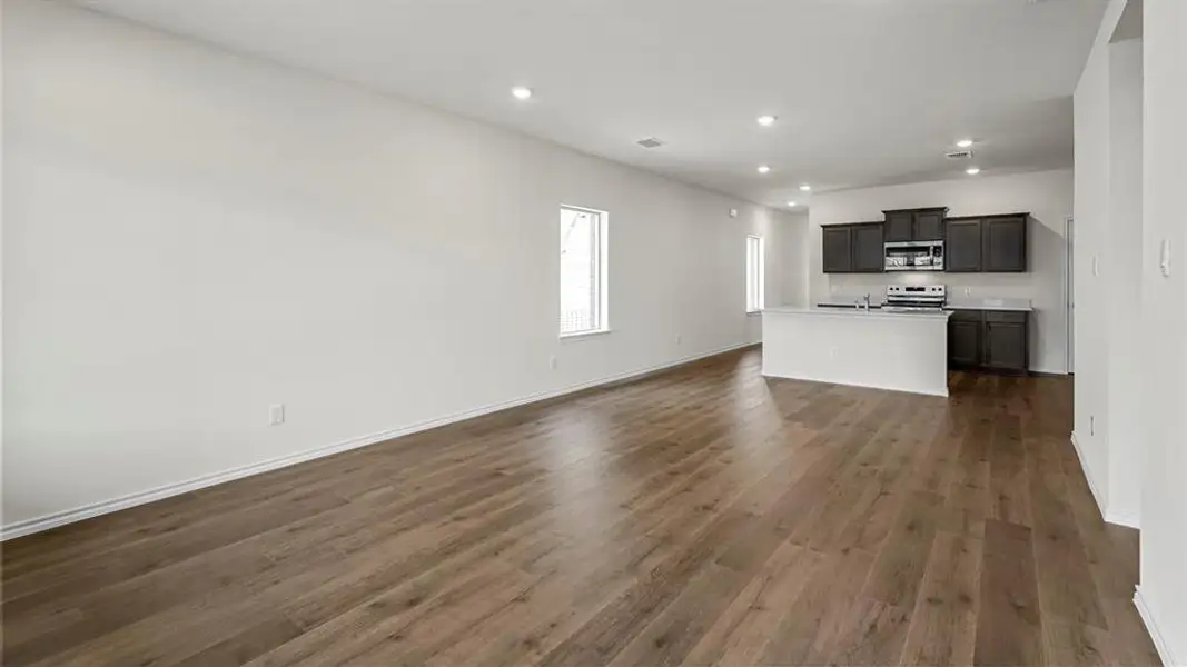 The main living area features wide plank flooring, recessed lighting, and a kitchen with dark cabinetry and stainless steel appliances