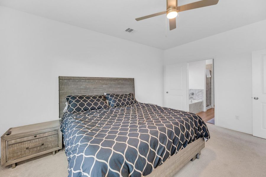 Bedroom featuring ensuite bath, a ceiling fan, visible vents, and carpet floors