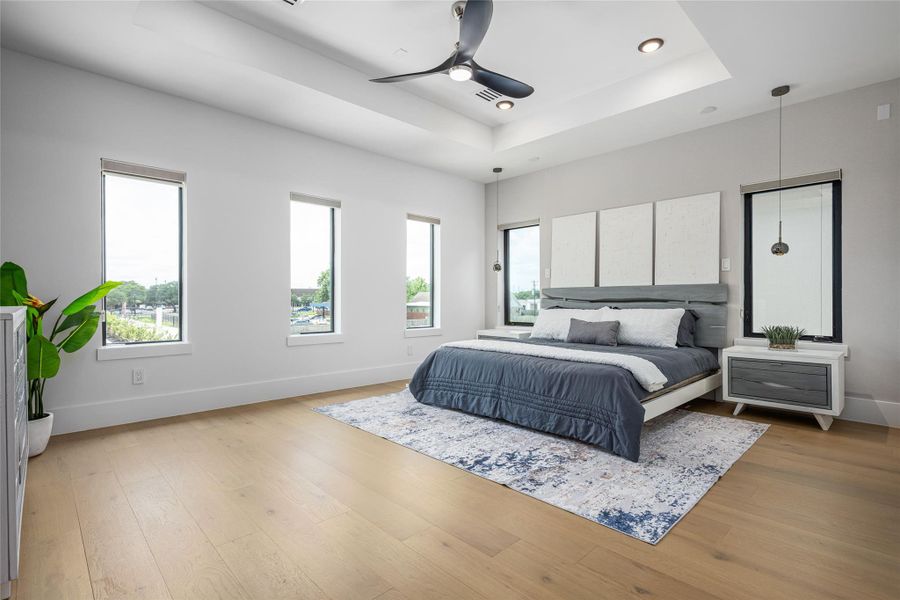 The primary bedroom is a sunlit sanctuary, complete with elegant wood floors, tray ceiling, and a thoughtfully designed custom closet The primary bedroom is a sunlit sanctuary, complete with elegant wood floors, tray ceiling, and a thoughtfully designed custom closet