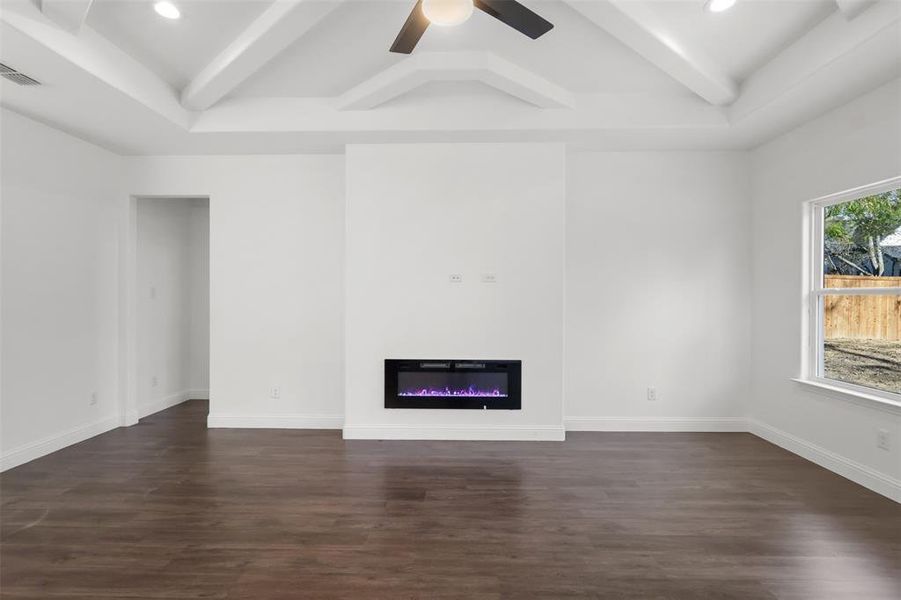 Unfurnished living room featuring beam ceiling, dark hardwood / wood-style flooring, and ceiling fan