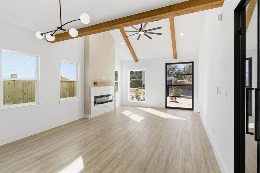 Unfurnished living room with vaulted ceiling, ceiling fan, light wood-style floors, and a glass covered fireplace