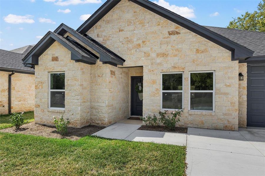 View of front facade featuring stone siding, a shingled roof, and a front yard