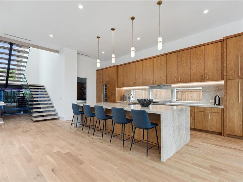 Kitchen with decorative light fixtures, light hardwood / wood-style floors, a spacious island, tasteful backsplash, and a breakfast bar