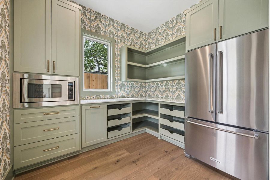 Custom walk in pantry featuring floor to ceiling cabinetry, built in drawer storage, open shelving, and designer wallpaper accents, offering abundant organization and prep space to complement the chef’s kitchen in this thoughtfully crafted Harvard Homes design.