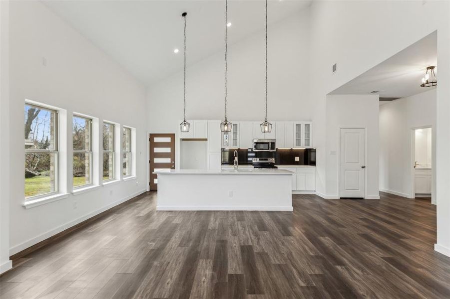 Kitchen featuring white cabinetry, stainless steel appliances, dark hardwood / wood-style floors, an island with sink, and decorative light fixtures