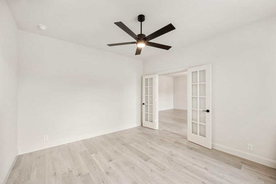 Empty room with light wood floors, black ceiling fan, and white French doors Empty room with light wood floors, black ceiling fan, and white French doors