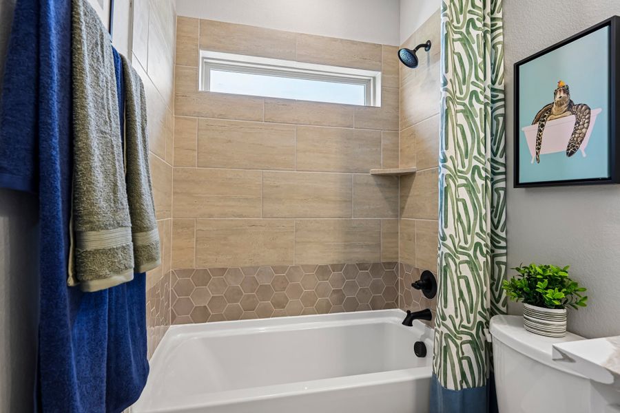 Bathroom with tiled shower and tub combo, green patterned curtain, small window, and decorative wall art