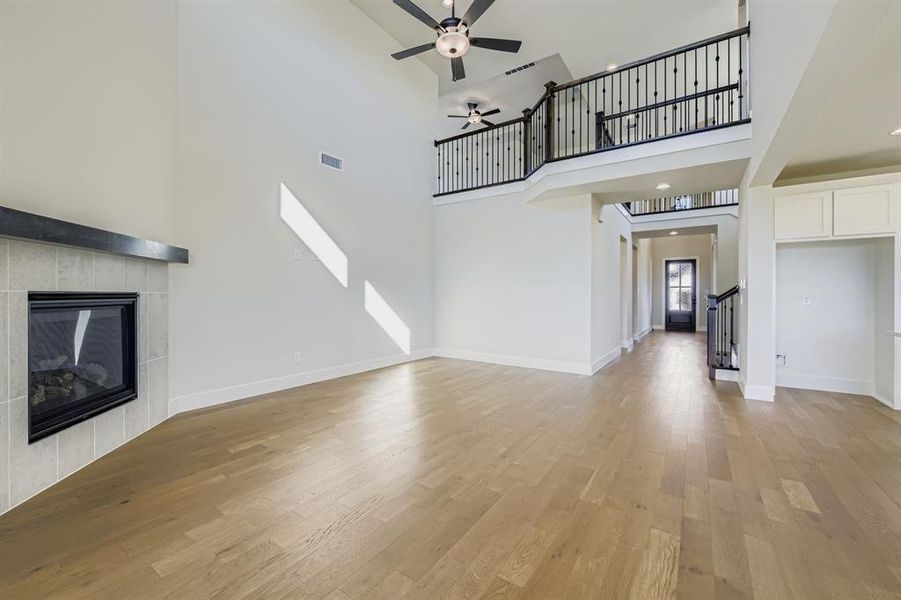 Unfurnished living room featuring a fireplace, light wood-style flooring, ceiling fan, a towering ceiling, and stairs