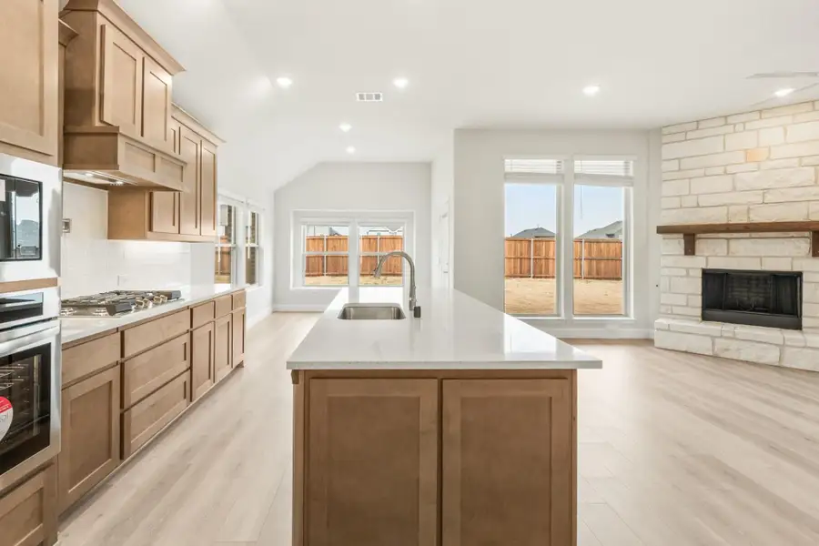 Kitchen with center island, wood cabinets, and stone fireplace visible in open living area Kitchen with center island, wood cabinets, and stone fireplace visible in open living area
