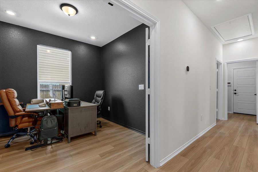 A dedicated home office provides a quiet space for productivity, complete with warm wood-look flooring and a window offering natural illumination.