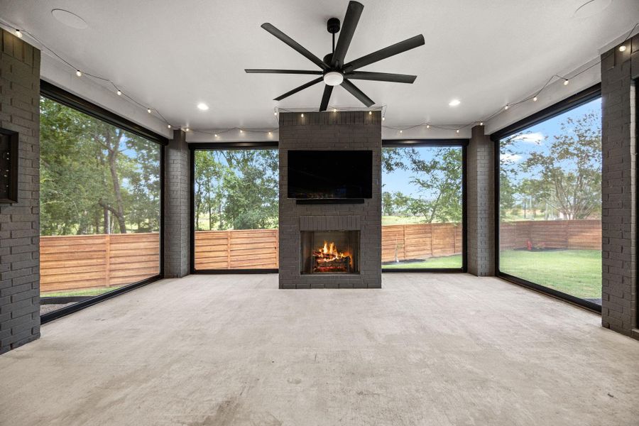 This spacious, enclosed patio features large windows offering scenic views, a central fireplace for cozy gatherings, and a ceiling fan for comfort. Ideal for relaxing or entertaining. This spacious, enclosed patio features large windows offering scenic views, a central fireplace for cozy gatherings, and a ceiling fan for comfort. Ideal for relaxing or entertaining.