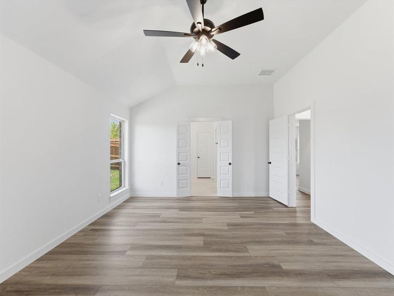 Spacious room featuring vaulted ceilings, wood-finish flooring, a contemporary ceiling fan with integrated lighting, and multiple paneled doors Spacious room featuring vaulted ceilings, wood-finish flooring, a contemporary ceiling fan with integrated lighting, and multiple paneled doors