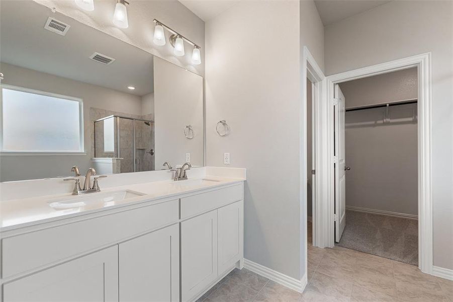 Bathroom with a walk in closet, a shower stall, double vanity, and light tile patterned floors Bathroom with a walk in closet, a shower stall, double vanity, and light tile patterned floors