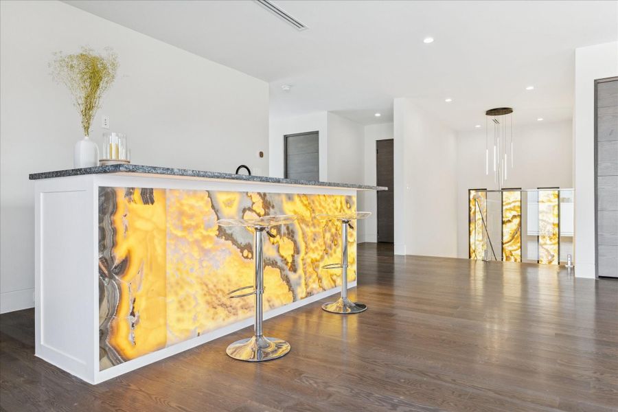 Third-floor game room with a stunning illuminated onyx bar and elegant dark wood floors.