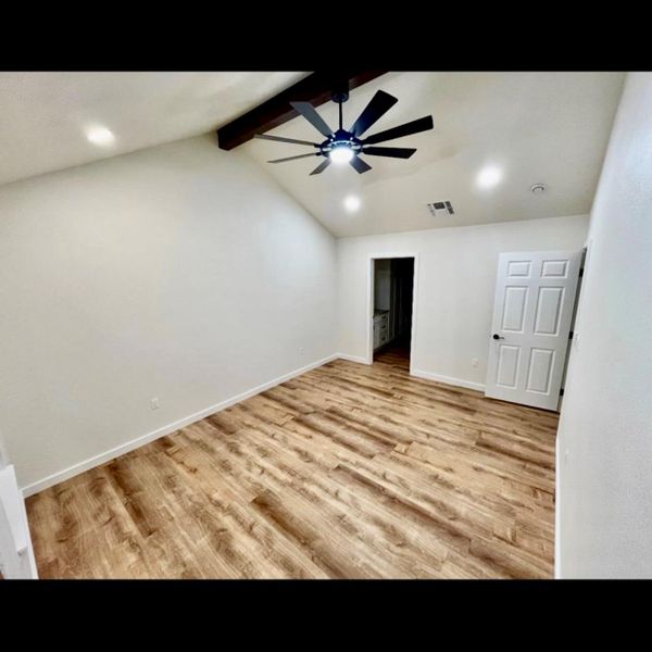 A well-lit bedroom features vaulted ceilings, rich wood-look flooring, and a modern ceiling fan.