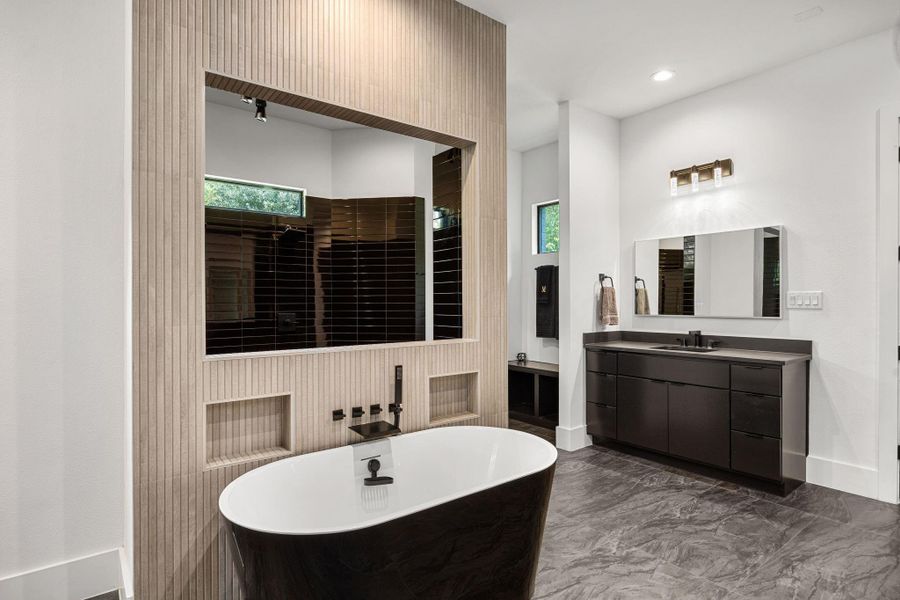 This modern bathroom features a sleek black freestanding tub. The space is brightened by recessed lighting and a contemporary wall fixture, with dark floor tiles adding a touch of elegance. This modern bathroom features a sleek black freestanding tub. The space is brightened by recessed lighting and a contemporary wall fixture, with dark floor tiles adding a touch of elegance.