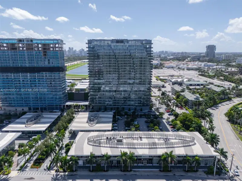 Aerial perspective of high-rise glass-facade towers featuring structured parking facilities with geometric roof patterns and integrated palm tree landscaping