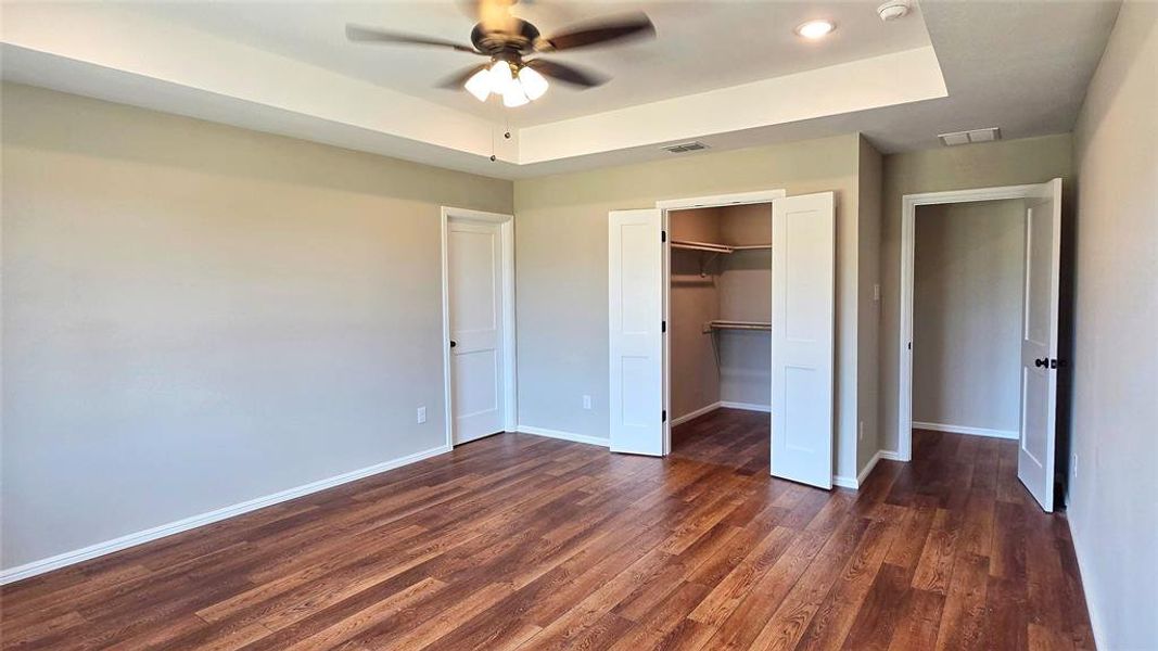 Unfurnished bedroom featuring a tray ceiling, dark wood-style floors, a spacious closet, and a ceiling fan