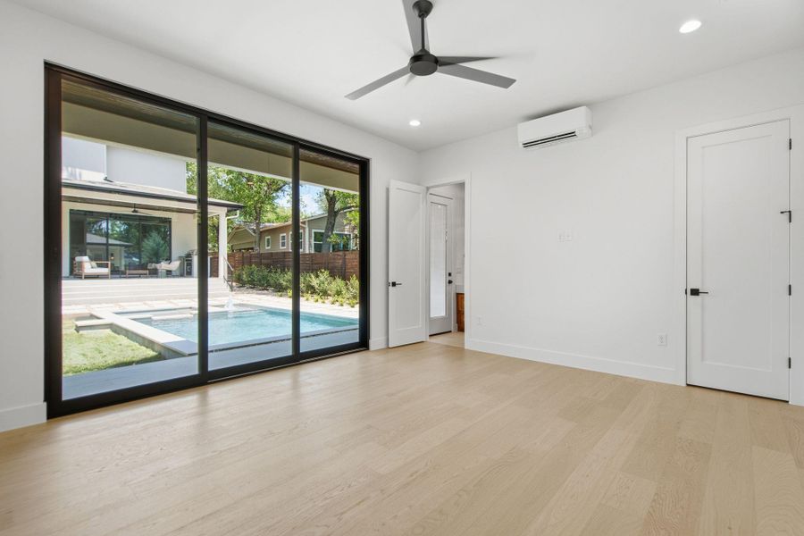 Massive sliding glass doors frame tranquil pool views from this light-filled room with wood flooring.