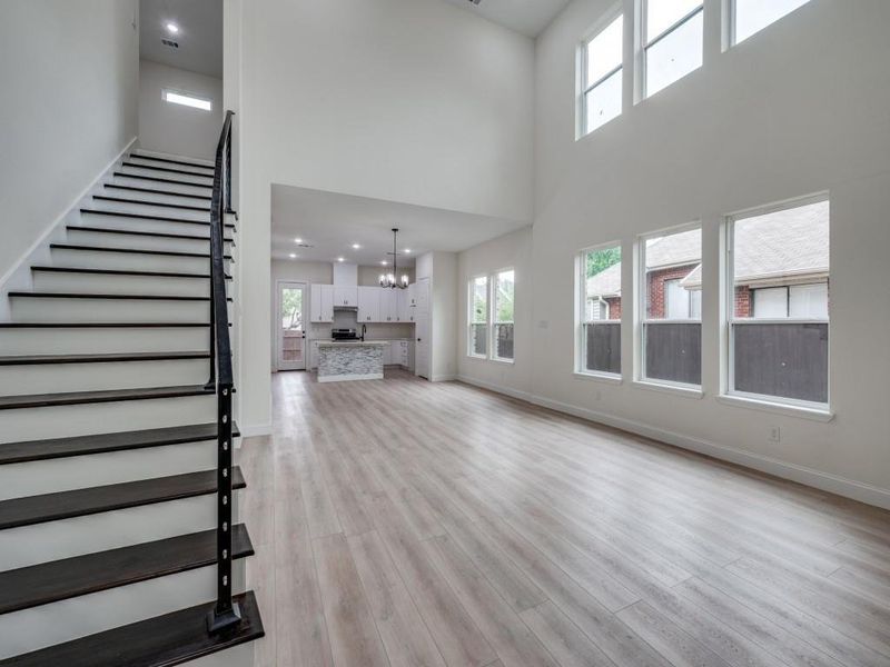 Unfurnished living room with a high ceiling, a chandelier, stairway, light wood-type flooring, and plenty of natural light