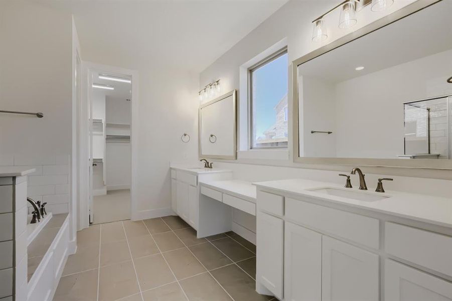 Bathroom featuring dual vanities with white cabinetry and countertops, framed mirrors, and bronze-finish fixtures