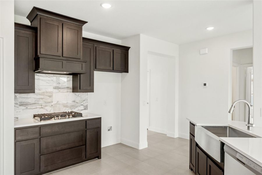 Kitchen with dark wood cabinets, marble backsplash, gas cooktop, and farmhouse sink with white countertops Kitchen with dark wood cabinets, marble backsplash, gas cooktop, and farmhouse sink with white countertops