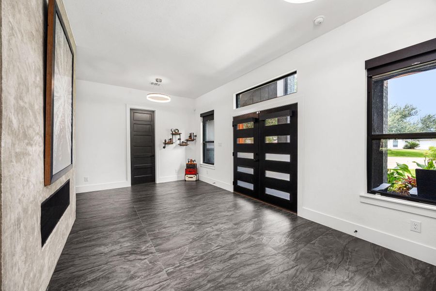 This spacious entryway features modern flooring, a sleek black front door with decorative glass panels, and large windows that provide natural light. The white walls and contemporary light fixture add a clean, stylish touch. This spacious entryway features modern flooring, a sleek black front door with decorative glass panels, and large windows that provide natural light. The white walls and contemporary light fixture add a clean, stylish touch.