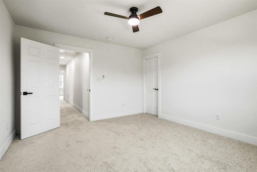 Carpeted room with white walls, a ceiling fan with wood-finish blades, and white paneled doors with black hardware Carpeted room with white walls, a ceiling fan with wood-finish blades, and white paneled doors with black hardware
