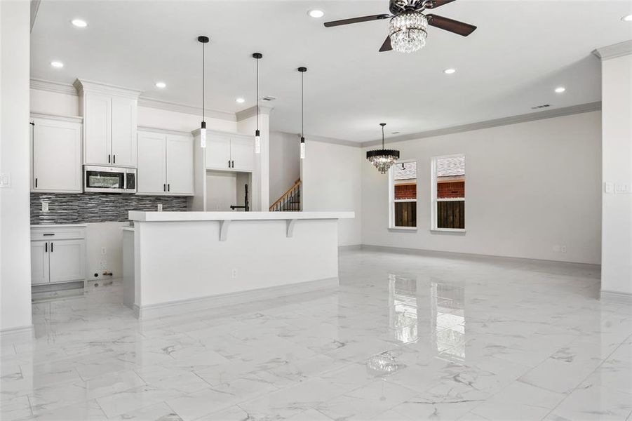 Kitchen with Quartz Counters, crown molding, light finish floors, tasteful backsplash, a center island, and stainless steel microwave Kitchen with Quartz Counters, crown molding, light finish floors, tasteful backsplash, a center island, and stainless steel microwave