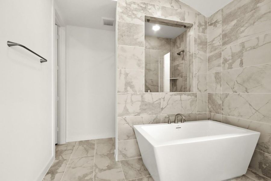 Spa-like primary bathroom showcasing floor-to-ceiling tile behind a freestanding tub, with a walk-in shower featuring a window that frames views into the tub area, creating a bright and open retreat.