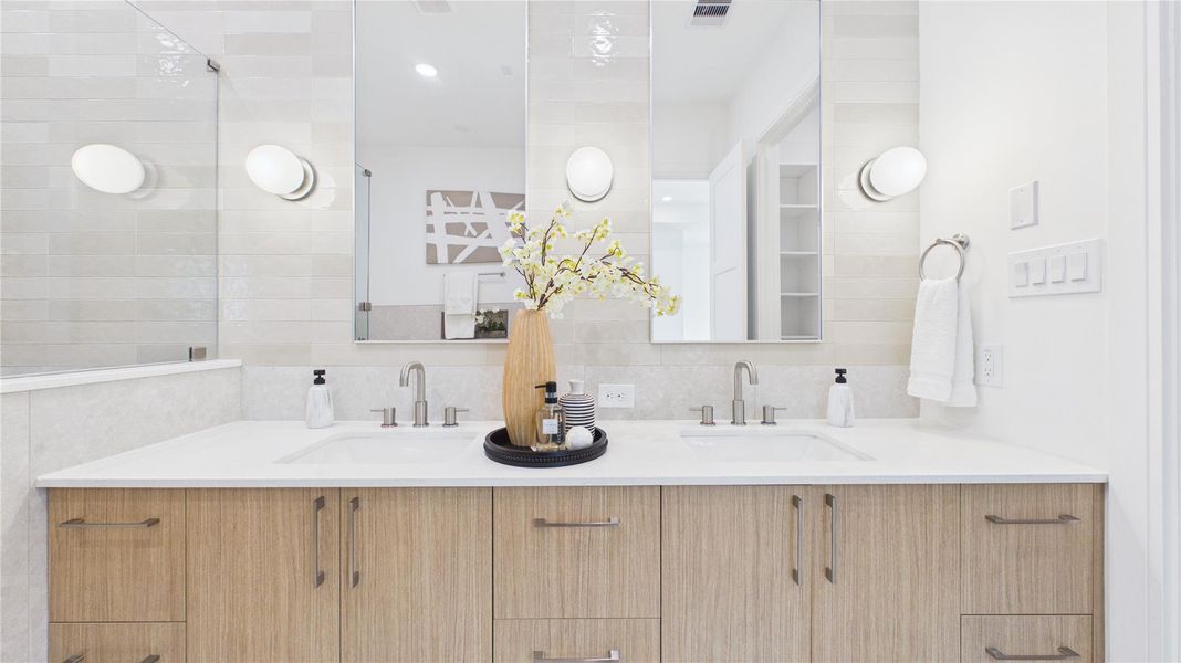 This modern bathroom features a double vanity with sleek wood cabinets, large mirrors, and soft lighting. The neutral tones and elegant fixtures create a clean, inviting space perfect for a contemporary home.