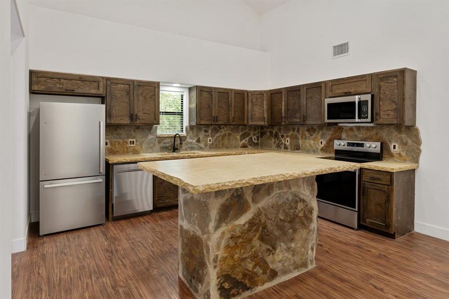 Kitchen with dark brown cabinets, backsplash, high vaulted ceiling, appliances with stainless steel finishes, and dark hardwood / wood-style floors