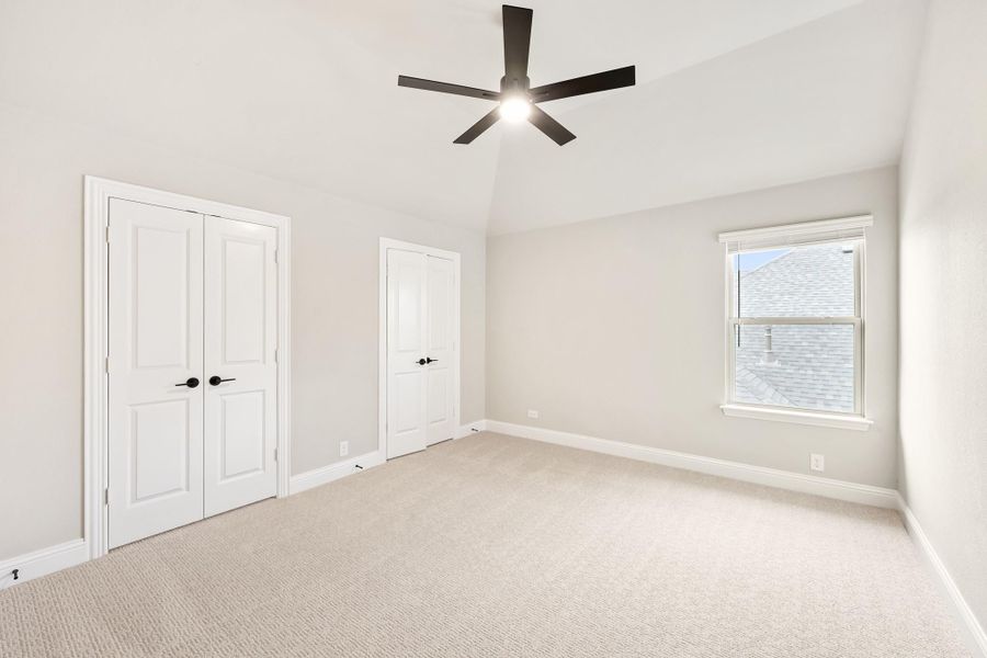 Empty bedroom with carpet, vaulted ceiling, black ceiling fan, double doors, and a window