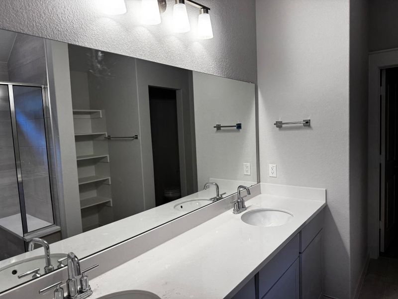 Full bath with a textured wall, a shower stall, and double vanity
