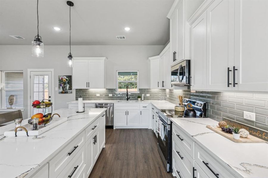 Kitchen with stainless steel appliances, light stone countertops, hanging light fixtures, white cabinetry, and recessed lighting