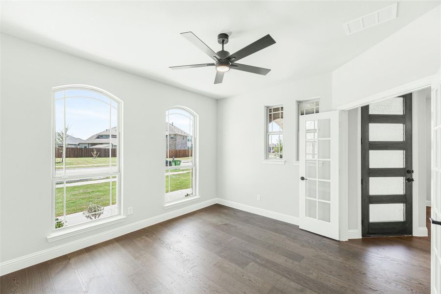 Bright empty room with dark hardwood floors, arched windows, ceiling fan, and dark wood front door with glass panels Bright empty room with dark hardwood floors, arched windows, ceiling fan, and dark wood front door with glass panels
