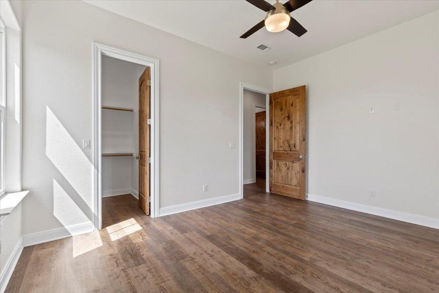 Unfurnished bedroom with wood finished floors, a walk in closet, a ceiling fan, and a closet